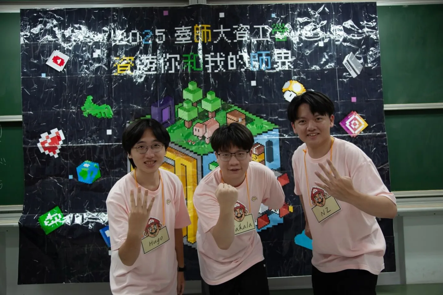 2025 臺師大資工營 3 位工作人員穿著營服,站在「資遊你和我的師界」主視覺背板前。